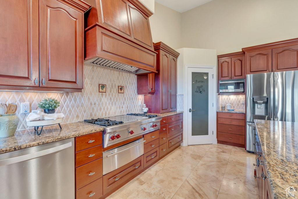 Kitchen featuring stainless steel appliances, a warming drawer, light stone counters, and backsplash