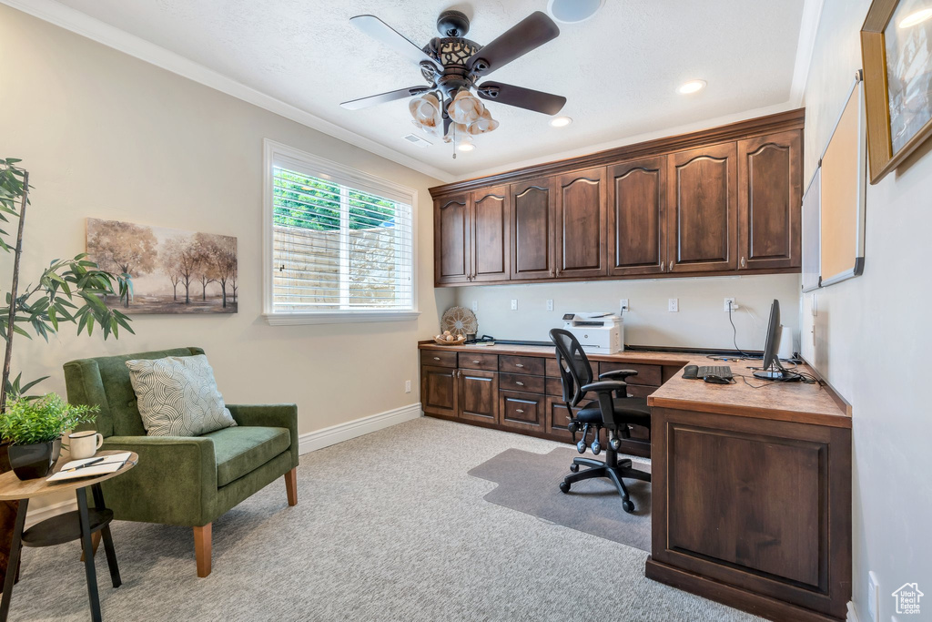 Office space with light colored carpet, ornamental molding, baseboards, ceiling fan, and built in desk