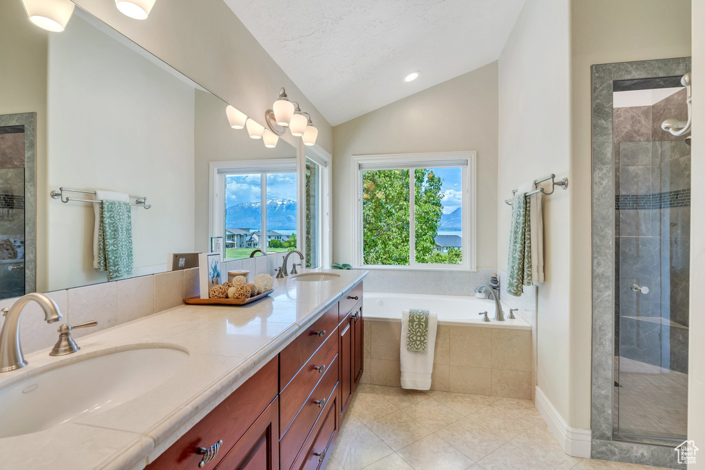 Bathroom featuring lofted ceiling, double vanity, a bath, tile patterned floors, and a stall shower