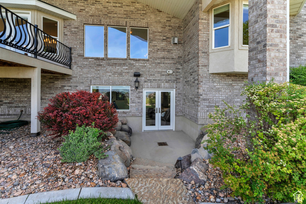 View of exterior entry featuring french doors, a balcony, and brick siding