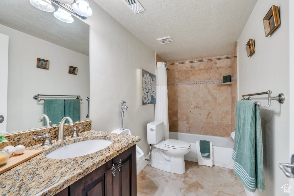 Full bathroom featuring vanity, toilet, shower / tub combo, and a textured ceiling