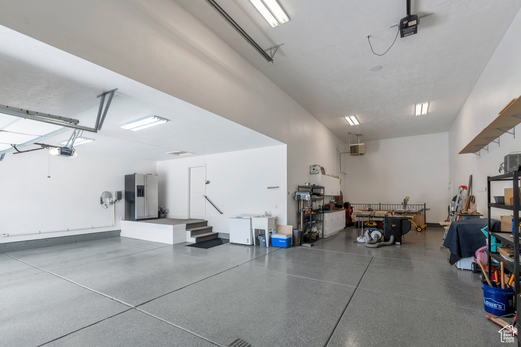Garage featuring a garage door opener and stainless steel refrigerator with ice dispenser