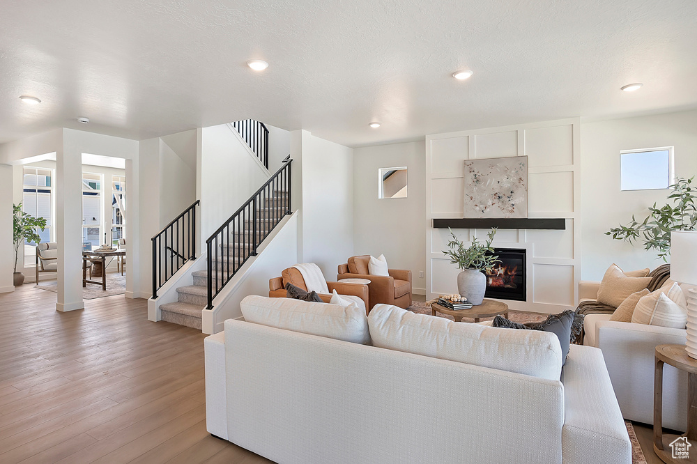 Living area with light wood finished floors, a glass covered fireplace, baseboards, stairs, and recessed lighting