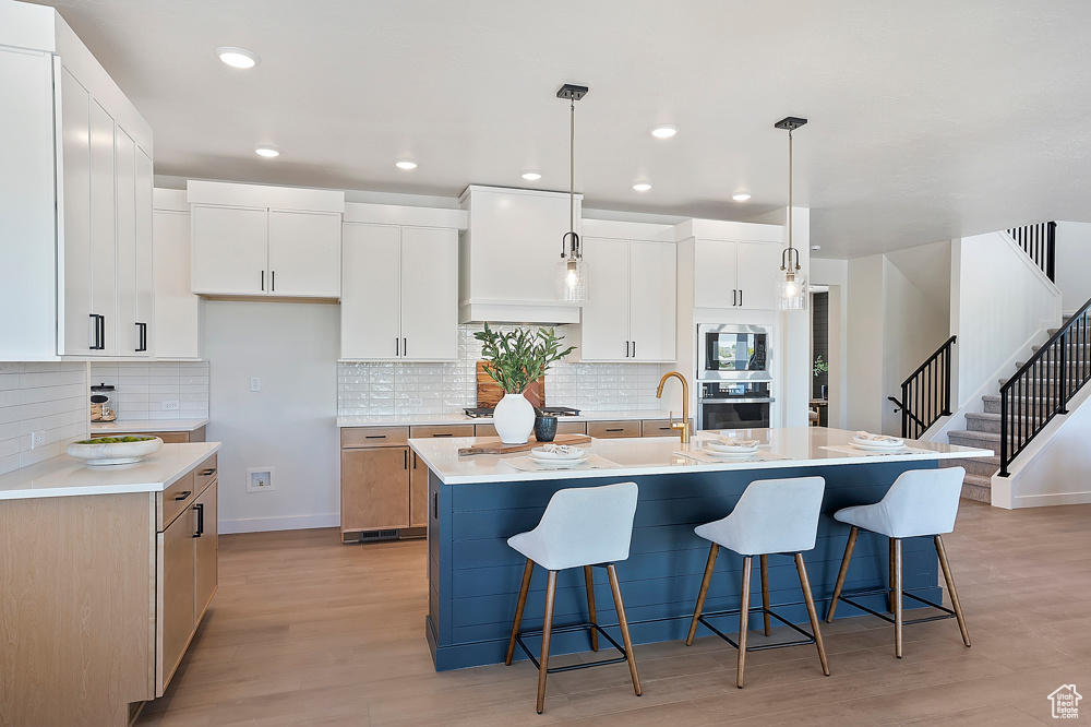 Kitchen featuring custom range hood, light wood-style flooring, a breakfast bar area, tasteful backsplash, and recessed lighting