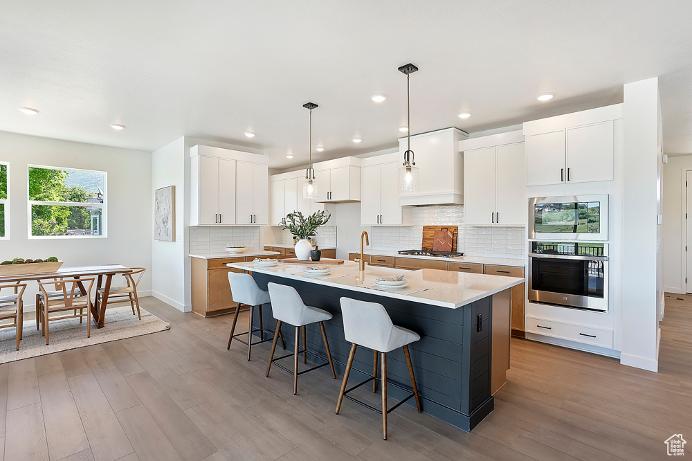 Kitchen featuring stainless steel appliances, a kitchen bar, light wood-type flooring, tasteful backsplash, and recessed lighting