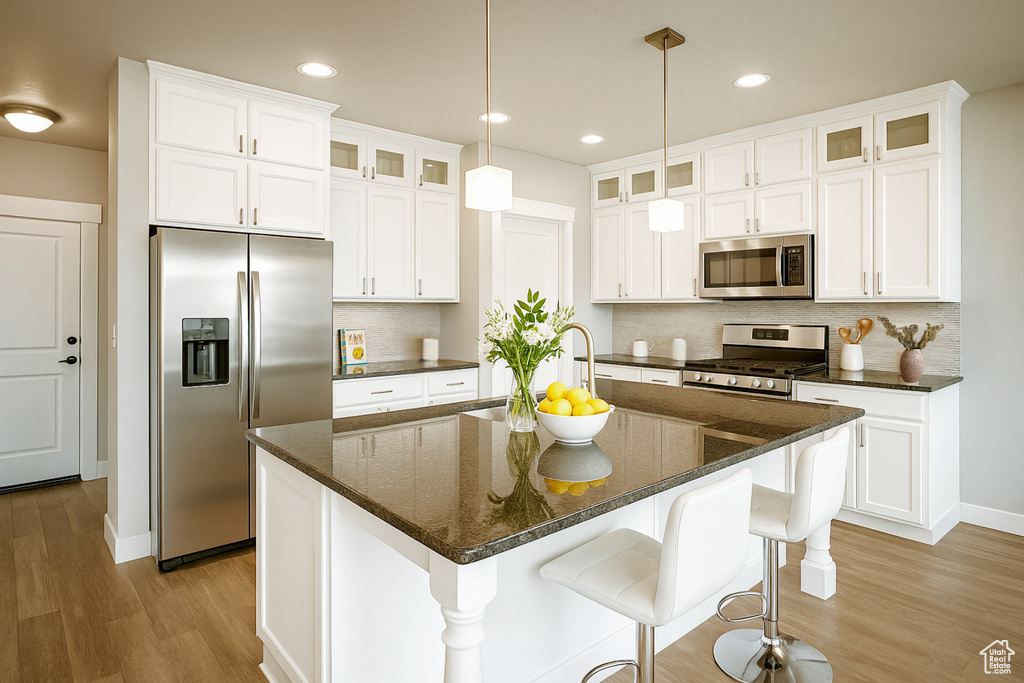Kitchen featuring stainless steel appliances, light wood finished floors, backsplash, white cabinets, and recessed lighting