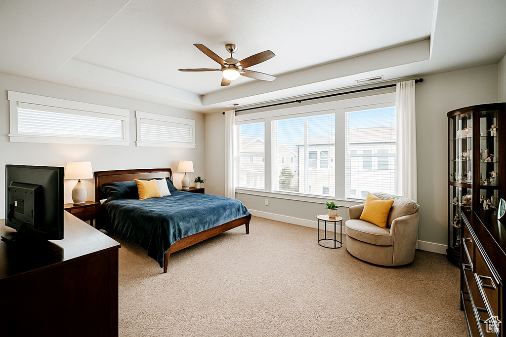 Bedroom featuring a raised ceiling, light carpet, baseboards, and a ceiling fan