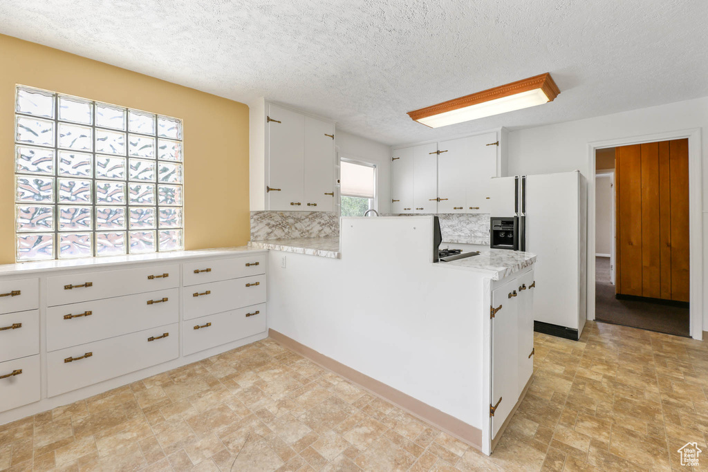Kitchen with white fridge with ice dispenser, decorative backsplash, light countertops, white cabinetry, and a peninsula