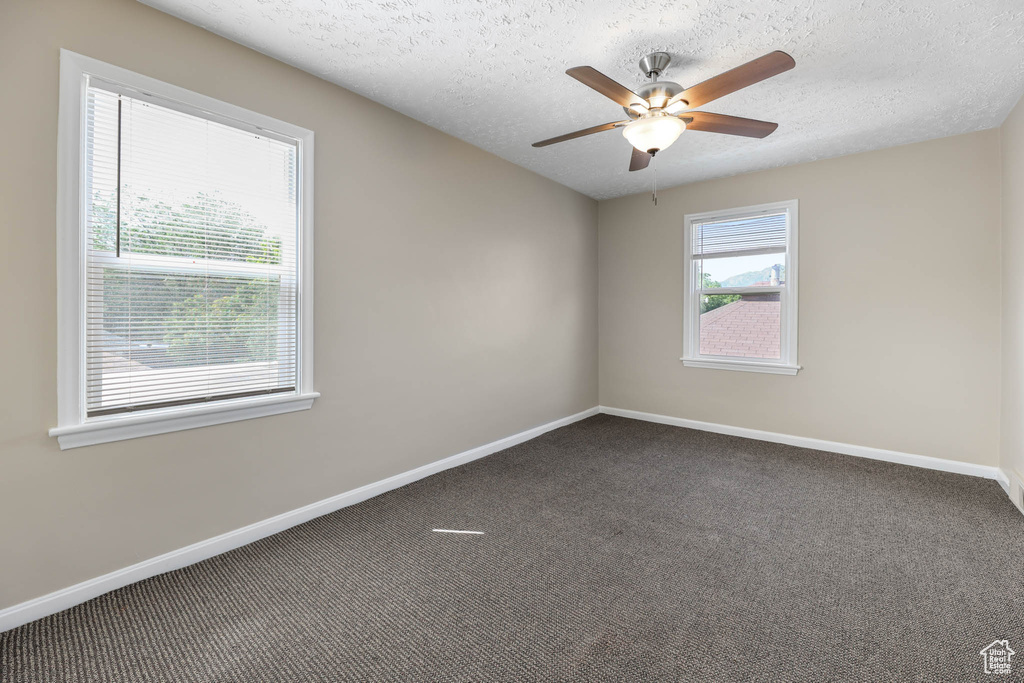 Empty room featuring carpet floors, baseboards, ceiling fan, and a textured ceiling
