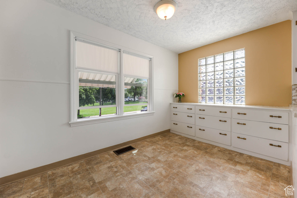 Unfurnished room featuring plenty of natural light, a textured ceiling, and baseboards