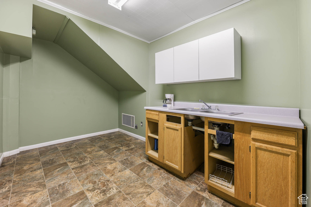 Kitchen with ornamental molding, baseboards, a sink, light countertops, and dark stone finish floors