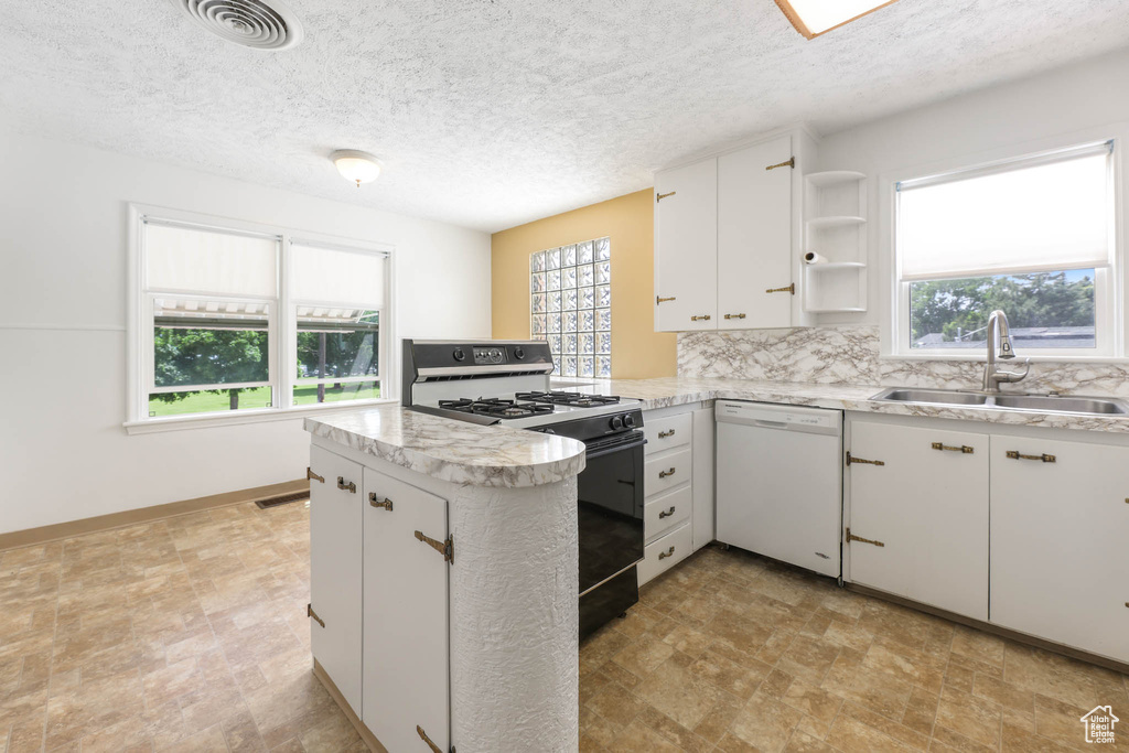 Kitchen featuring white dishwasher, gas stove, a sink, a peninsula, and healthy amount of natural light