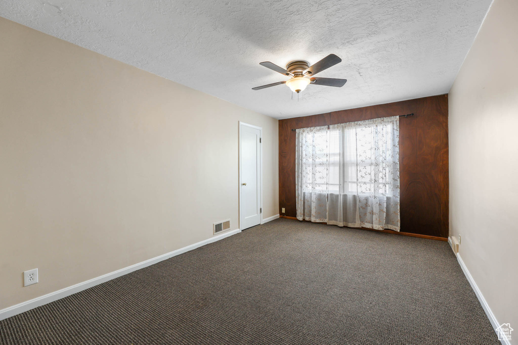 Empty room with ceiling fan, baseboards, a textured ceiling, and dark carpet