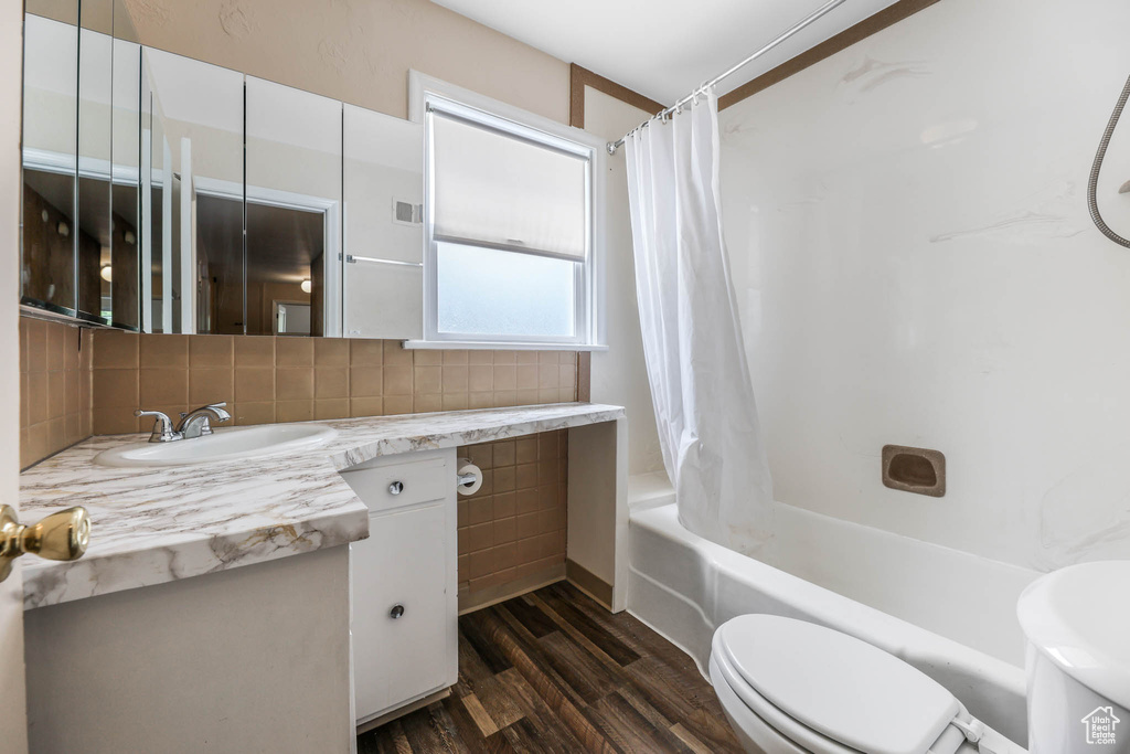 Bathroom featuring toilet, vanity, wood finished floors, shower / bath combo with shower curtain, and decorative backsplash