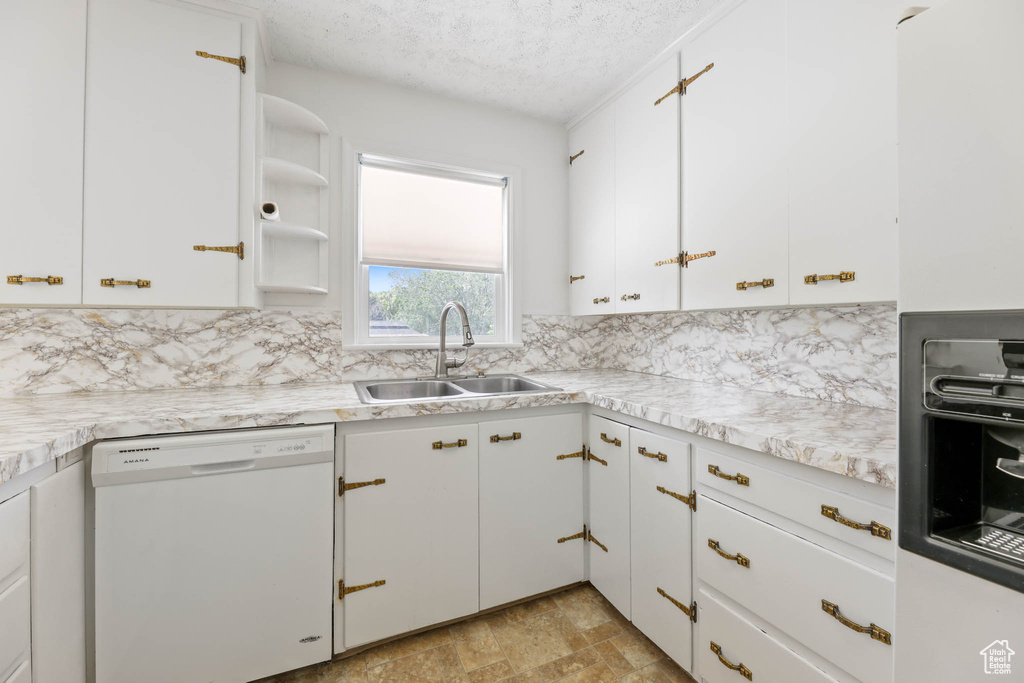 Kitchen featuring white dishwasher, a sink, a textured ceiling, light countertops, and backsplash