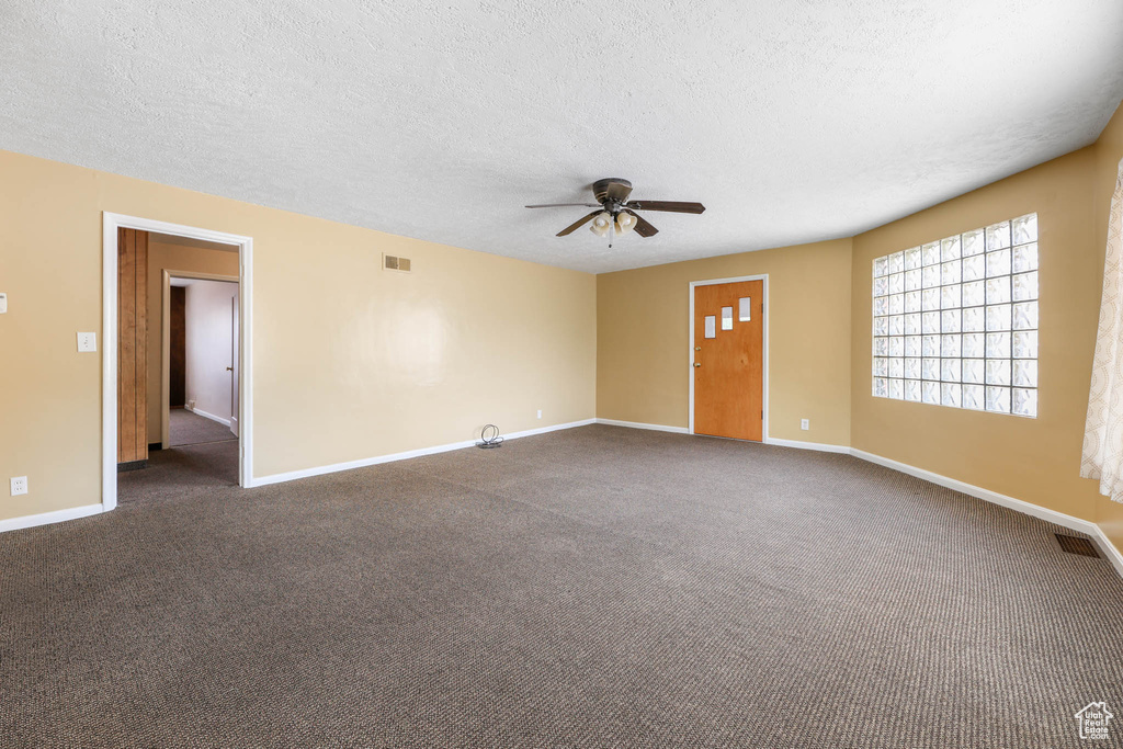 Empty room with a textured ceiling, ceiling fan, baseboards, and dark carpet