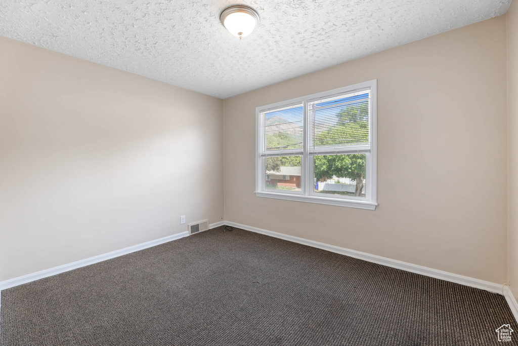 Spare room featuring dark colored carpet, a textured ceiling, and baseboards