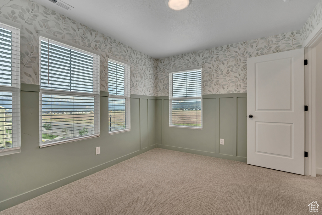 Empty room with wallpapered walls, wainscoting, a decorative wall, and carpet flooring