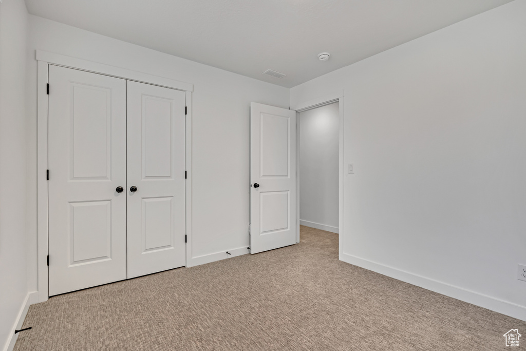 Unfurnished bedroom with light carpet, baseboards, and a closet