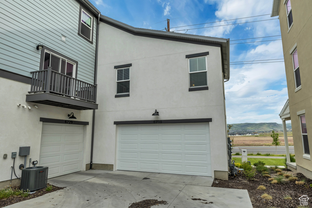 Back of property featuring a garage, a balcony, central AC, stucco siding, and a mountain view