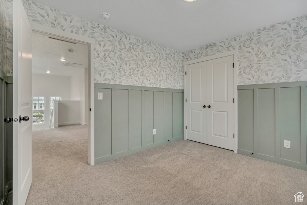 Unfurnished bedroom featuring wallpapered walls, wainscoting, carpet, and a decorative wall