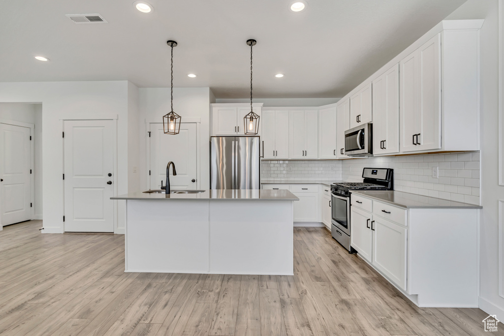 Kitchen with stainless steel appliances, a sink, a center island with sink, tasteful backsplash, and light wood-type flooring