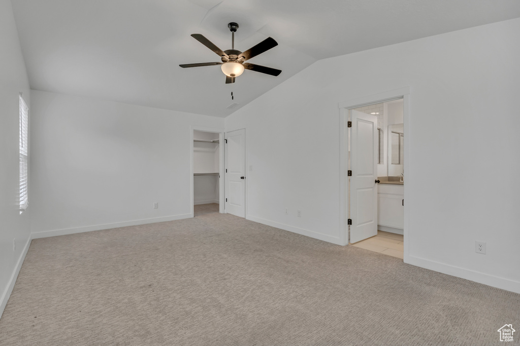 Unfurnished bedroom with lofted ceiling, light carpet, baseboards, a spacious closet, and connected bathroom