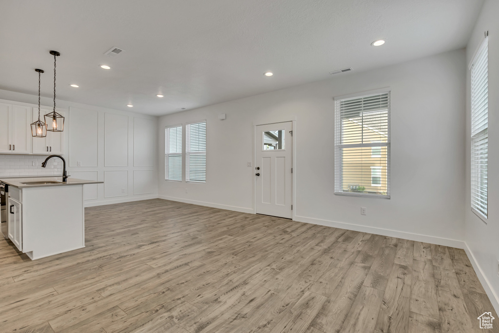 Kitchen with a sink, light wood-type flooring, white cabinets, pendant lighting, and light countertops