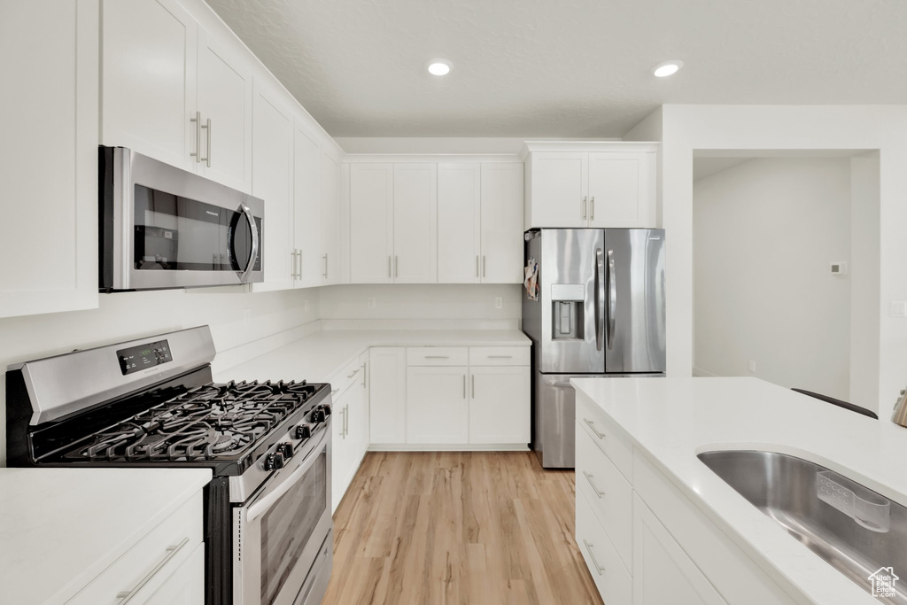 Kitchen featuring stainless steel appliances, a sink, light wood-style flooring, white cabinets, and light countertops