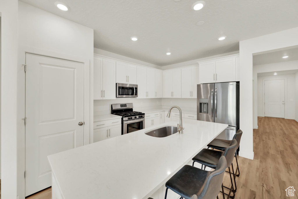 Kitchen featuring appliances with stainless steel finishes, a sink, light wood finished floors, a kitchen breakfast bar, and a kitchen island with sink