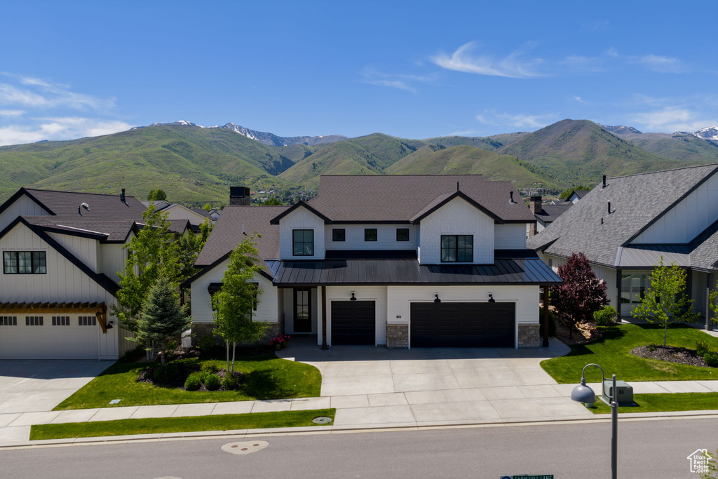 View of front of property featuring driveway, a standing seam roof, an attached garage, and a mountain view