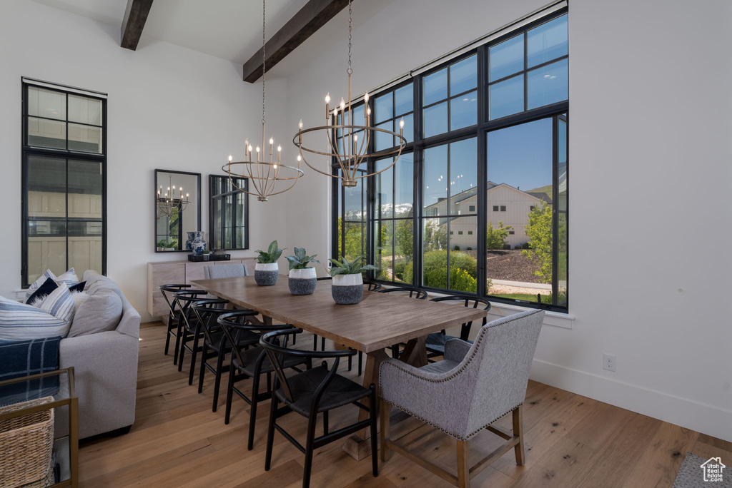 Dining space with a chandelier, beamed ceiling, a towering ceiling, wood finished floors, and baseboards