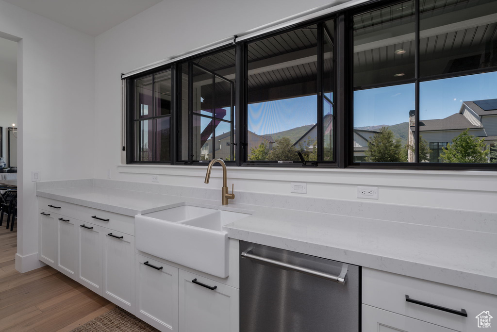 Kitchen featuring stainless steel dishwasher, a sink, light wood finished floors, and white cabinets