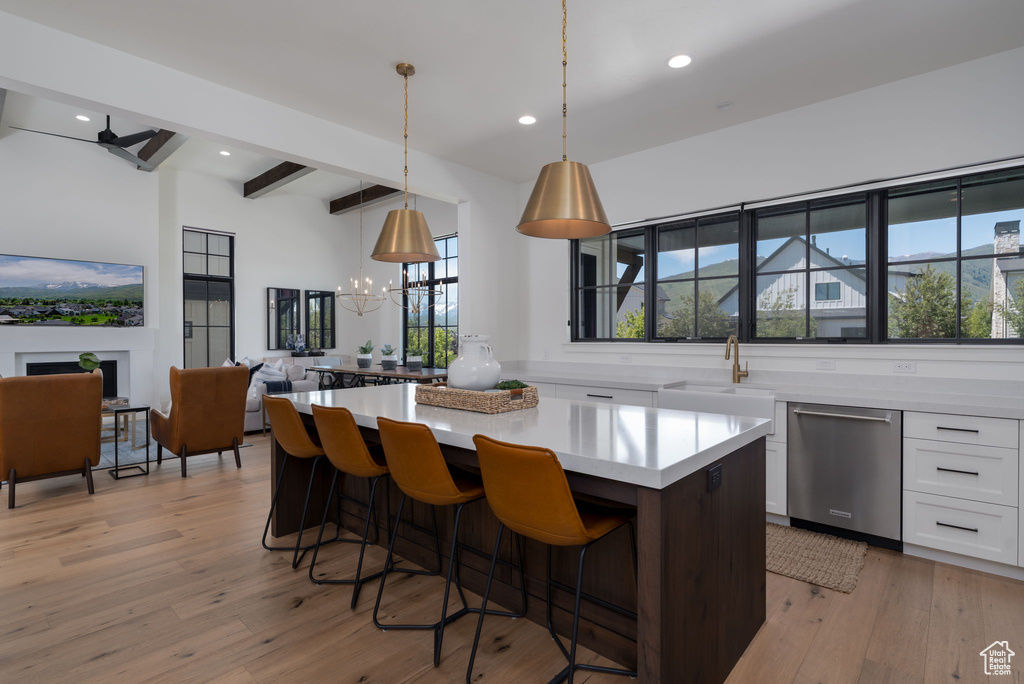 Kitchen with stainless steel dishwasher, a sink, white cabinetry, beamed ceiling, and a center island