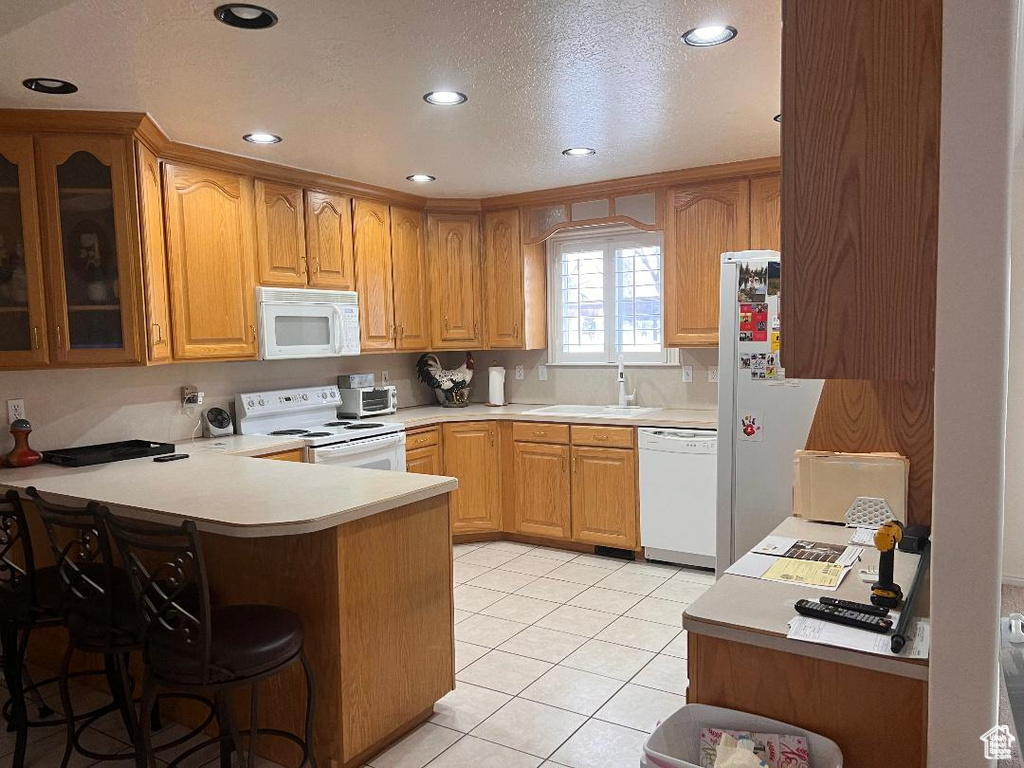 Kitchen featuring white appliances, a peninsula, a sink, a breakfast bar area, and glass insert cabinets