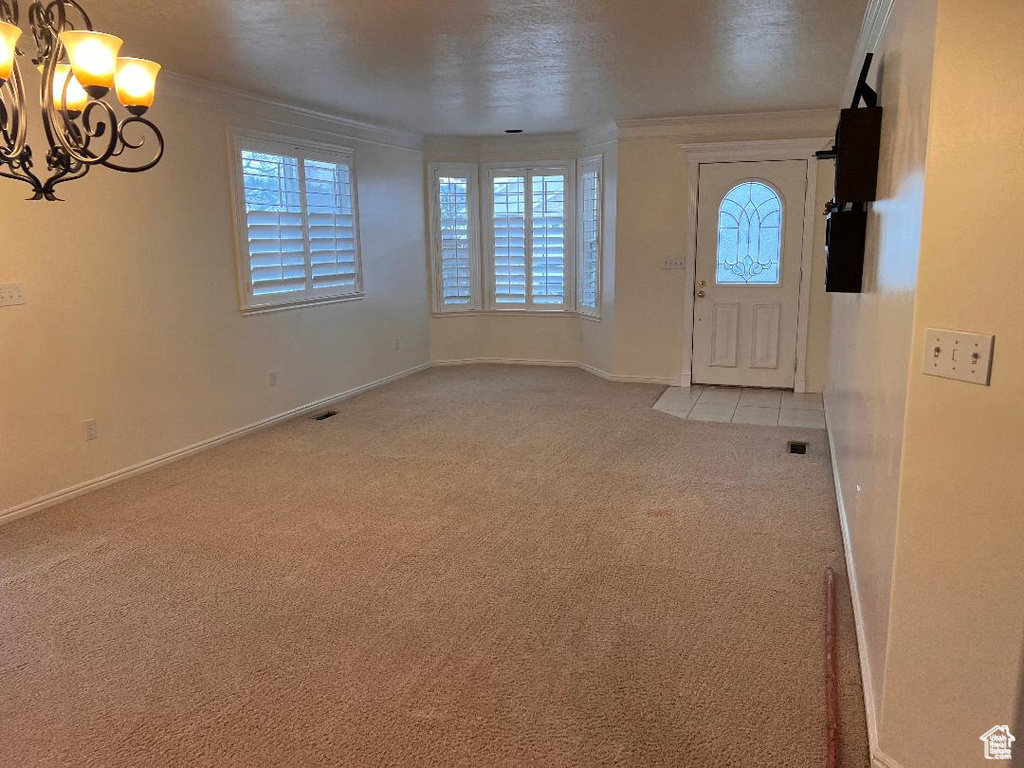 Carpeted entryway with a chandelier, ornamental molding, and baseboards