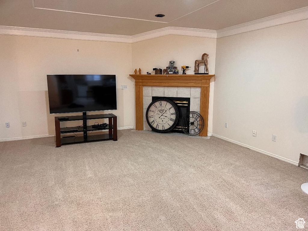 Living room featuring crown molding, carpet floors, baseboards, and a tiled fireplace