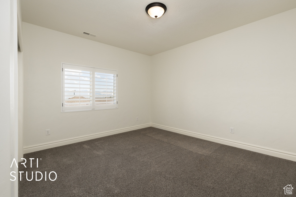 Unfurnished room featuring dark colored carpet and baseboards
