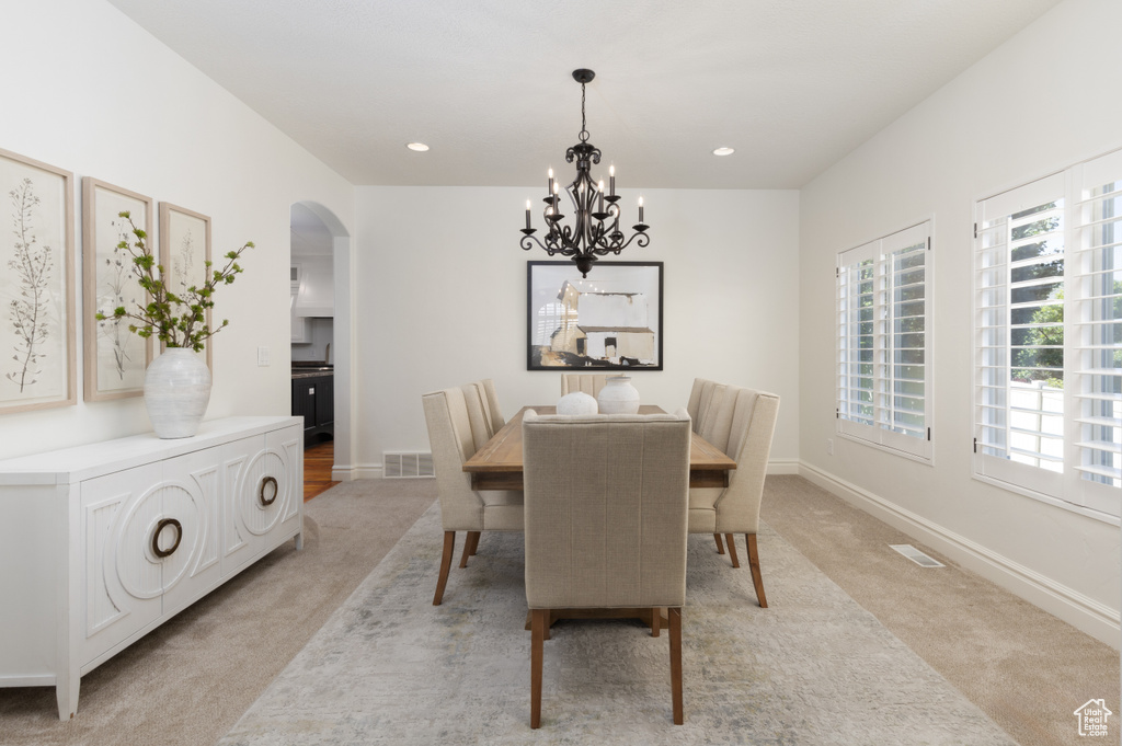 Dining area featuring light carpet, arched walkways, a chandelier, baseboards, and recessed lighting