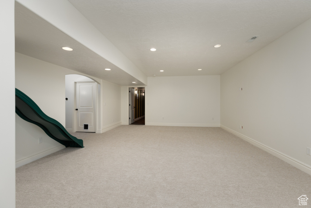 Basement with recessed lighting, light colored carpet, arched walkways, and baseboards