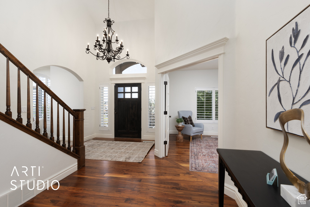 Entrance foyer featuring wood finished floors, a chandelier, arched walkways, a high ceiling, and stairway