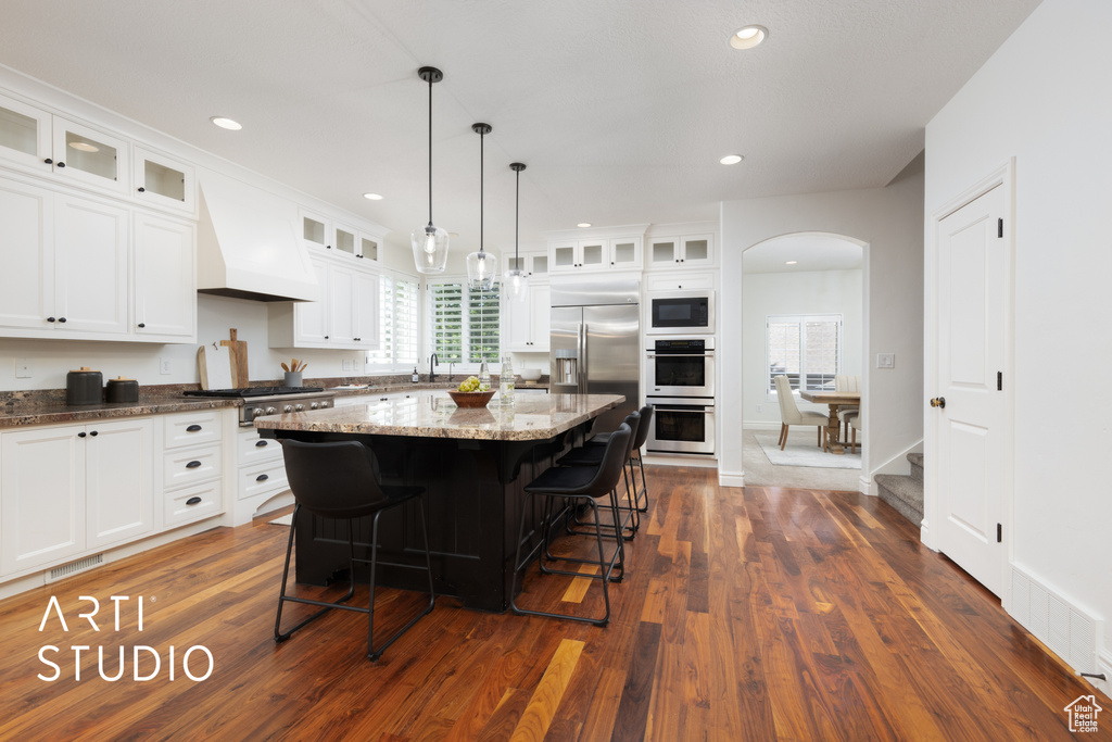 Kitchen with built in appliances, premium range hood, a kitchen breakfast bar, dark wood-style floors, and arched walkways