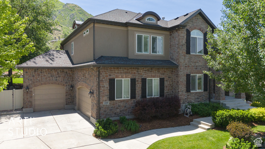 View of front of home featuring driveway, stucco siding, stone siding, and a garage