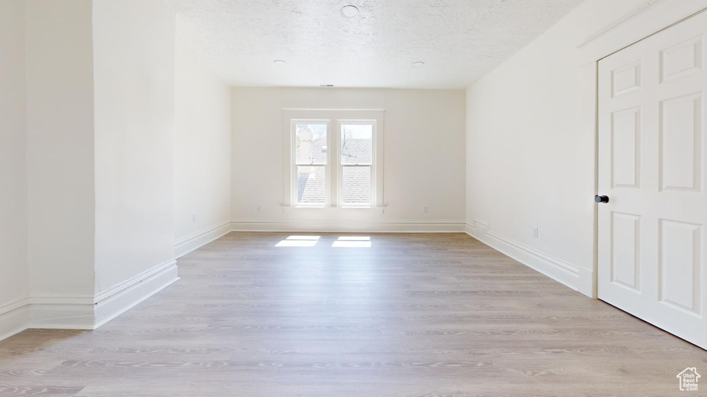 Spare room with light wood finished floors, baseboards, and a textured ceiling