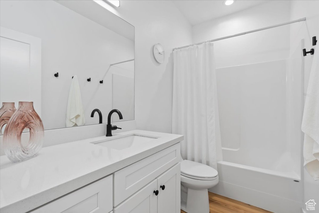 Full bath featuring vanity, wood finished floors, shower / bath combo, toilet, and recessed lighting