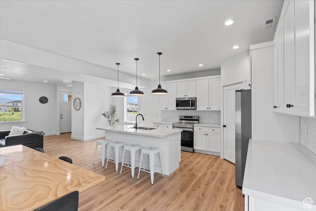 Kitchen featuring appliances with stainless steel finishes, backsplash, a sink, a breakfast bar, and light wood finished floors