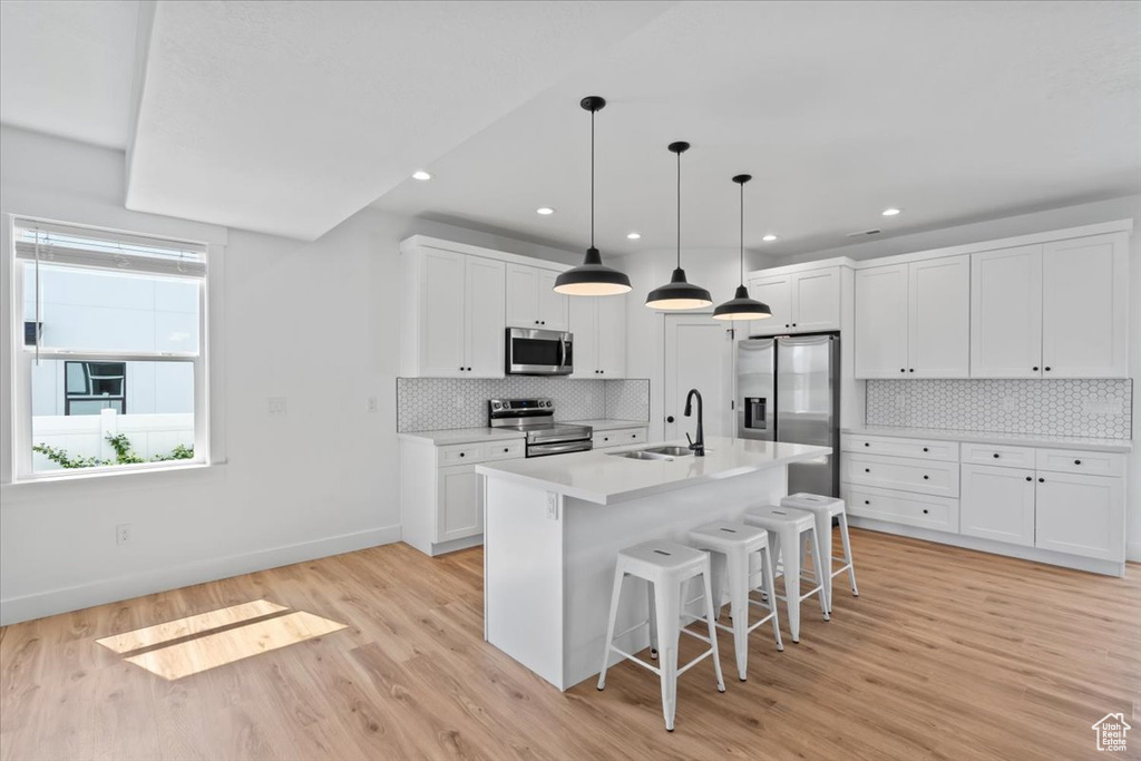 Kitchen with appliances with stainless steel finishes, a kitchen bar, a sink, light wood-style floors, and white cabinets