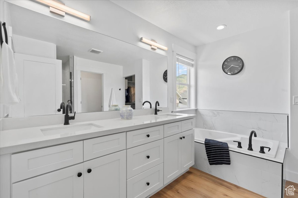 Full bath with double vanity, a garden tub, and wood finished floors