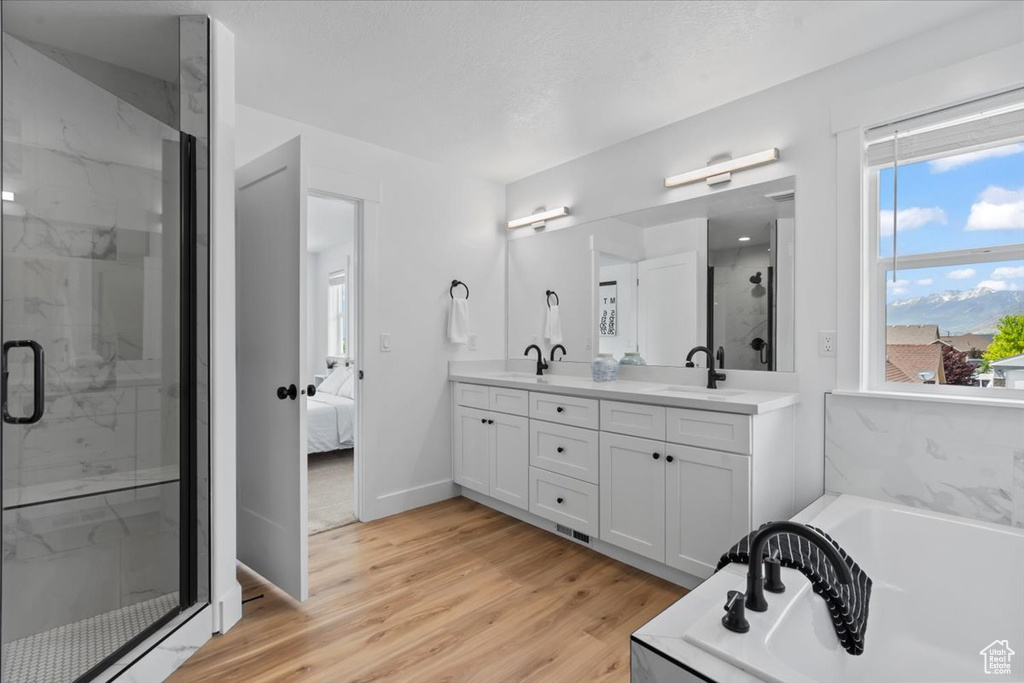 Full bath with double vanity, a bath, a marble finish shower, wood finished floors, and connected bathroom