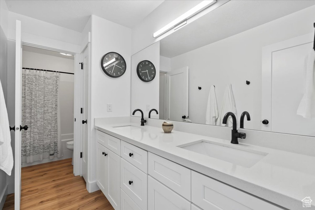 Full bathroom with double vanity, toilet, wood finished floors, and curtained shower